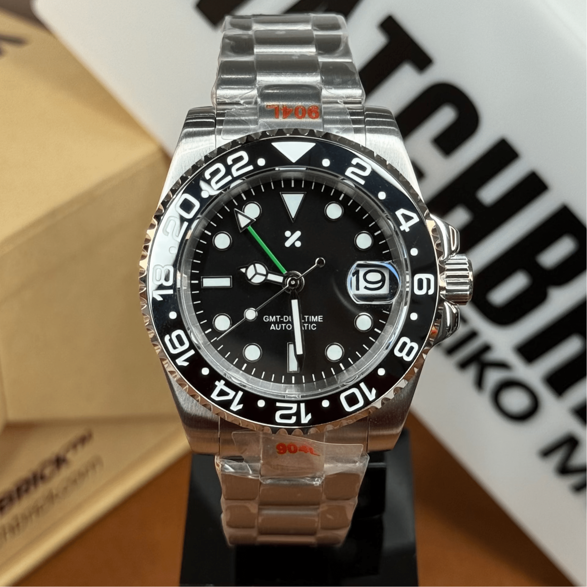 Stainless steel GMT automatic dive watch with black bezel and green GMT hand on display.