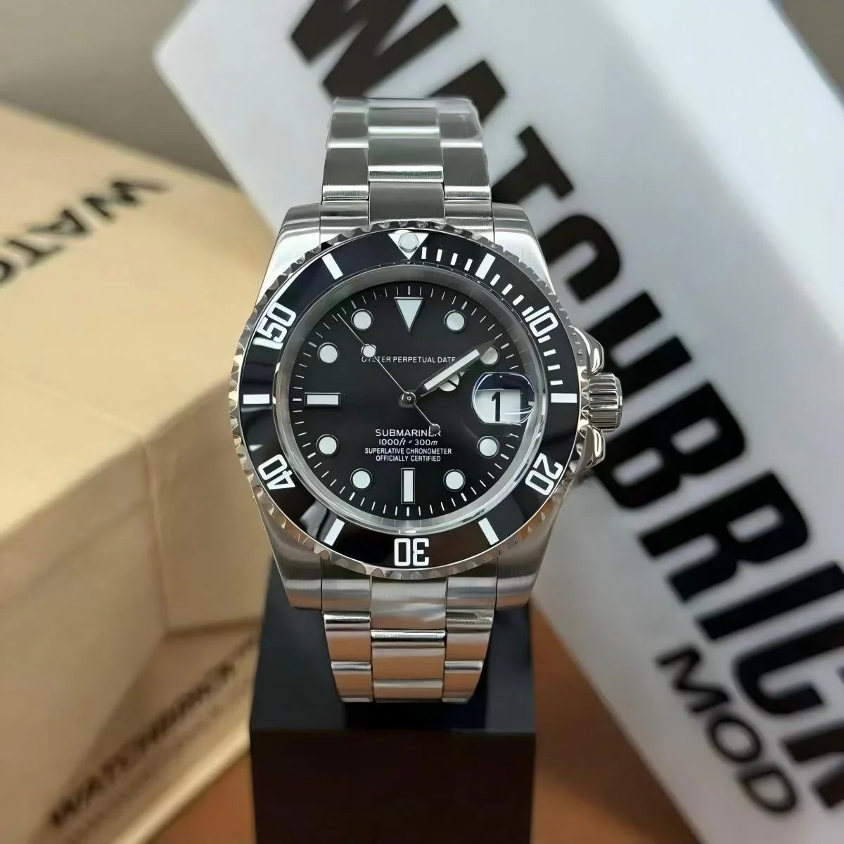 Stainless steel dive watch with black bezel, black dial, and date window on display stand