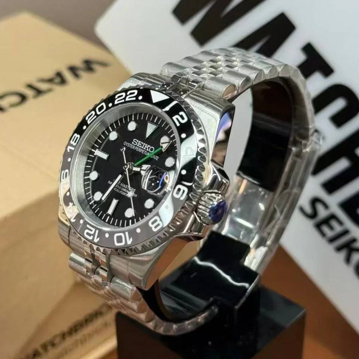 Seiko mod watch with black bezel, stainless steel bracelet, and black dial on display stand