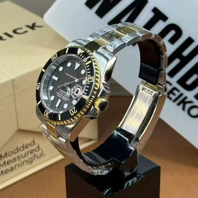 Custom Seiko mod watch with black and gold bezel, stainless steel bracelet, and sapphire crystal on display stand.