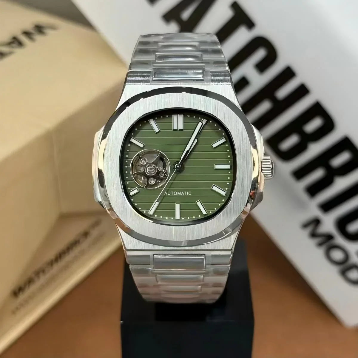 Silver stainless steel automatic watch with green dial and open-heart design on display stand