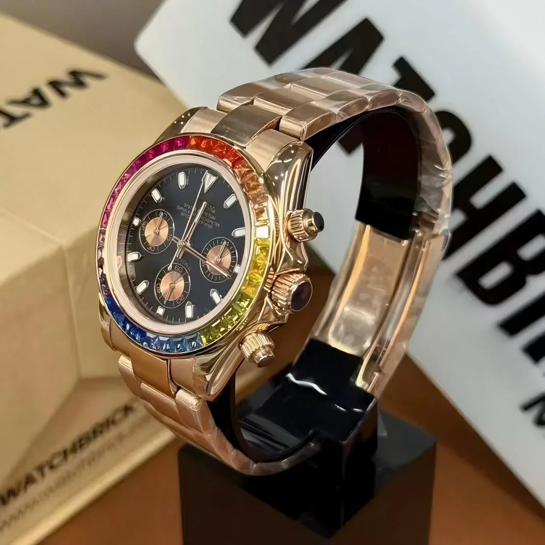 Rose gold chronograph watch with rainbow bezel and black dial, displayed on a stand