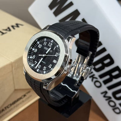 Black Seiko mod watch with silver bezel, black rubber strap, and date display on stand