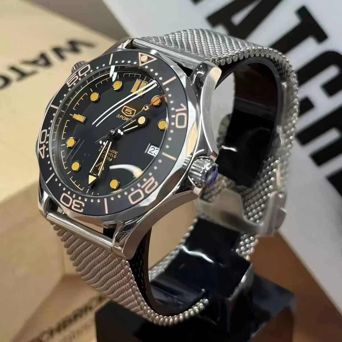 Seiko mod automatic dive watch with black bezel, yellow markers, and mesh stainless strap on display