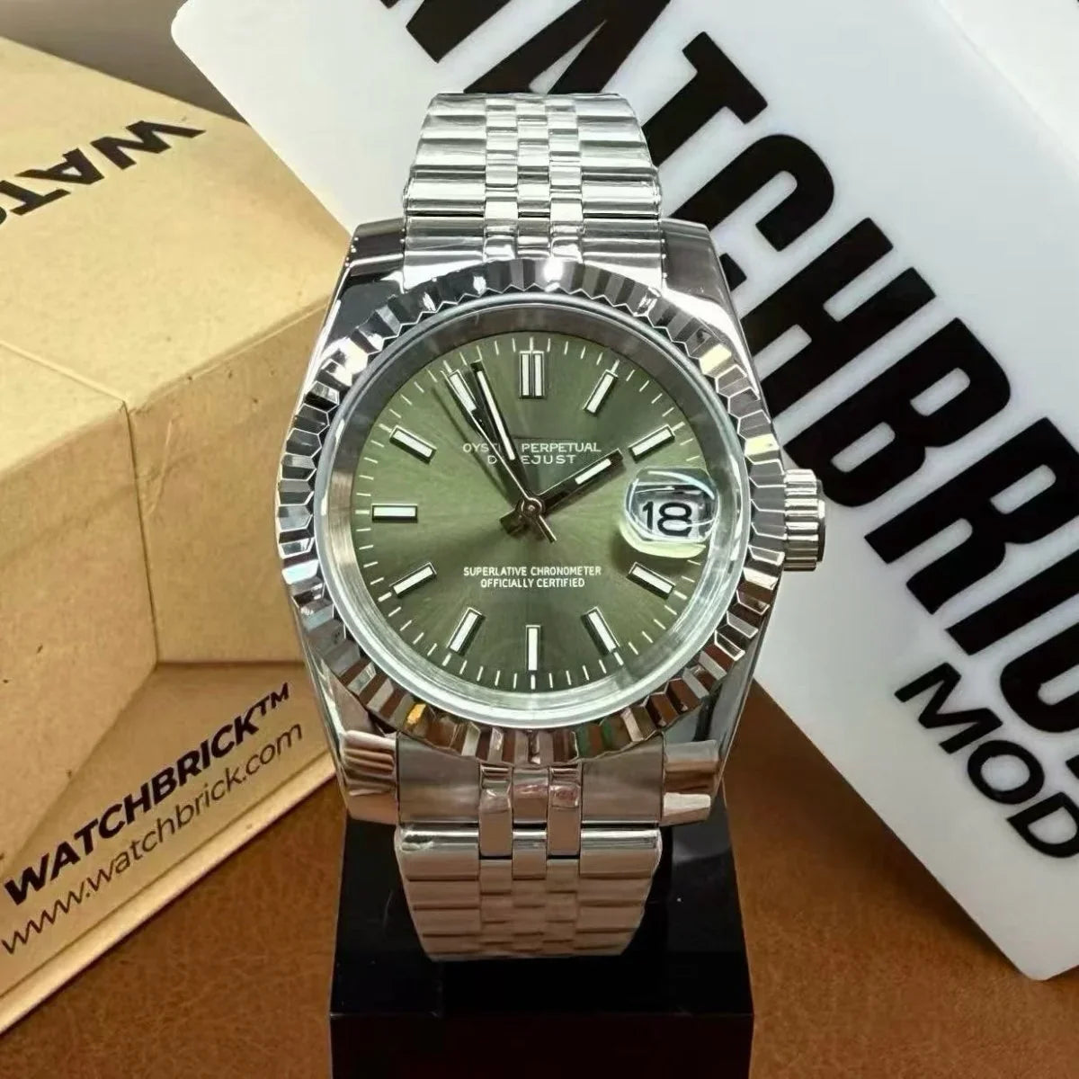 Stainless steel watch with green dial and date display, on a metal bracelet, displayed on stand