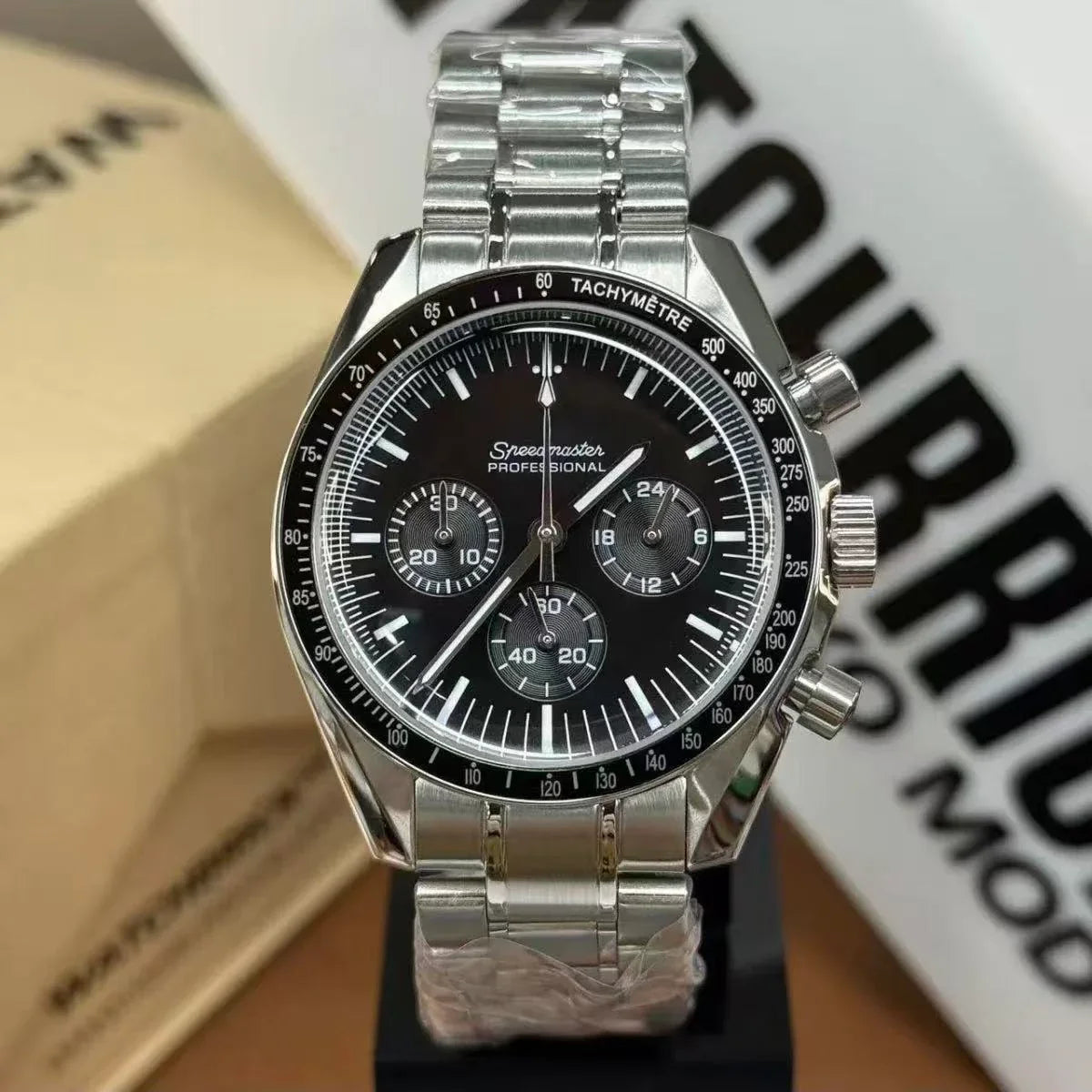 Stainless steel chronograph watch with black dial, tachymeter bezel, and metal bracelet on display.