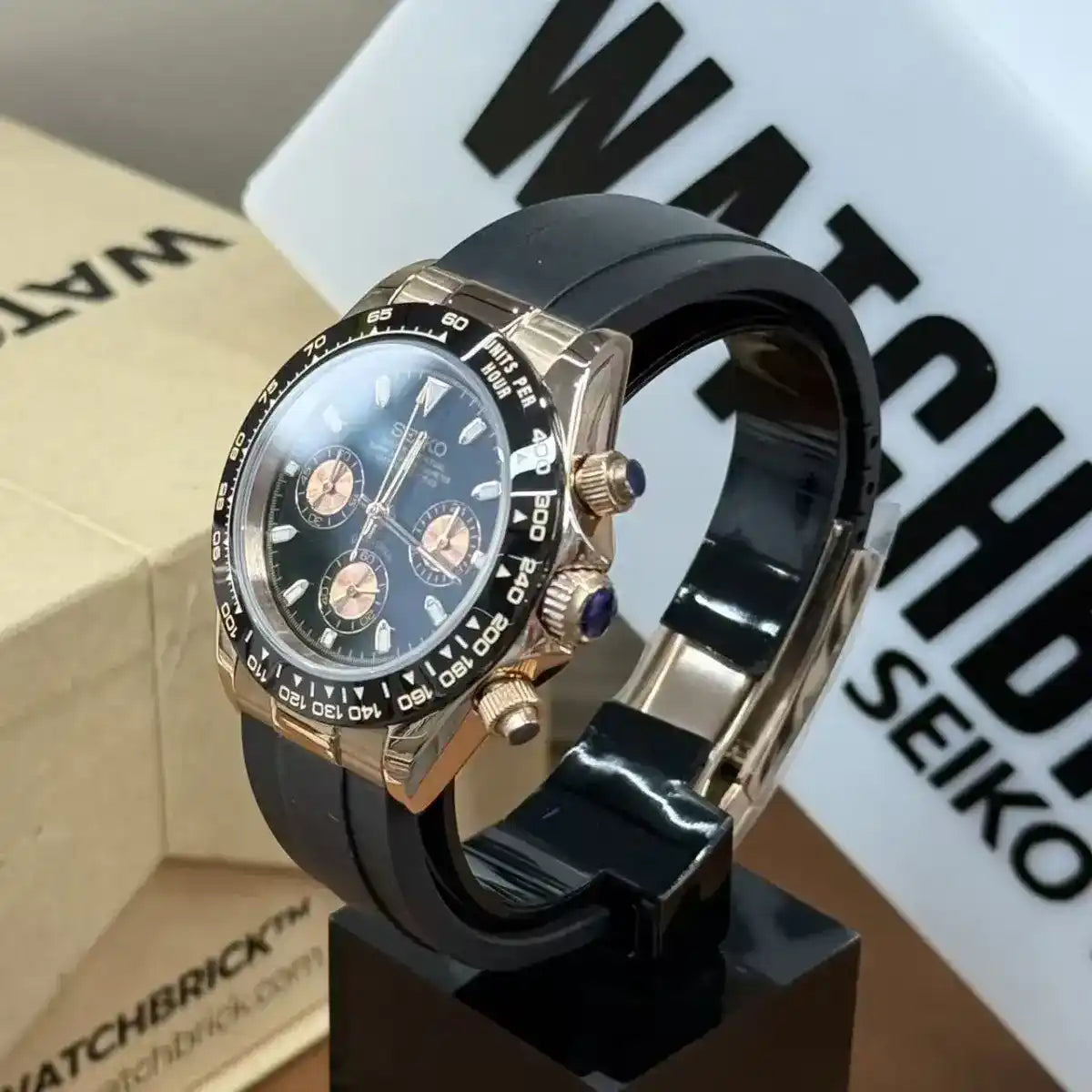 Rose gold Seiko VK63 chronograph watch with black dial, black rubber strap, and tachymeter bezel
